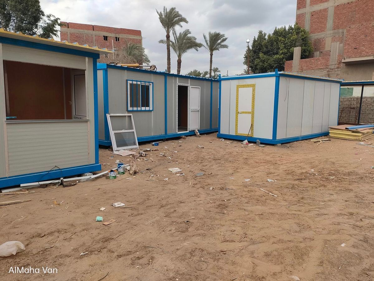 مجموعة كرفانات ساندوتش بانل بأبواب ملونة على أرض رملية بين النخيل