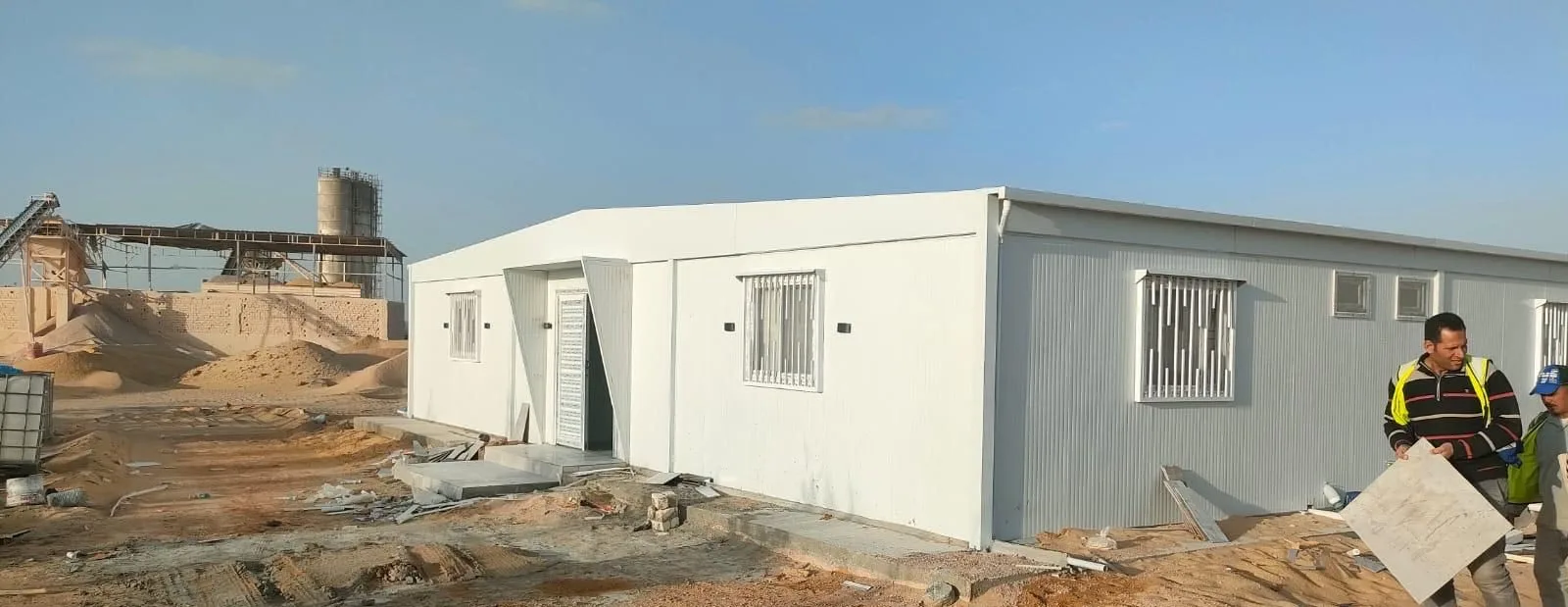 عمال شركة المها يركّبون مدخل مجمع كرفانات سكن عمال أبيض في موقع عمل صحراوي
