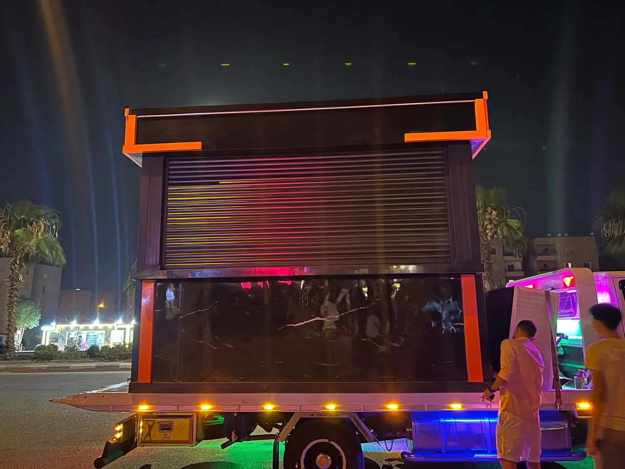 كشك مطعم أسود بإطار برتقالي محمّل على سيارة نقل ليلاً