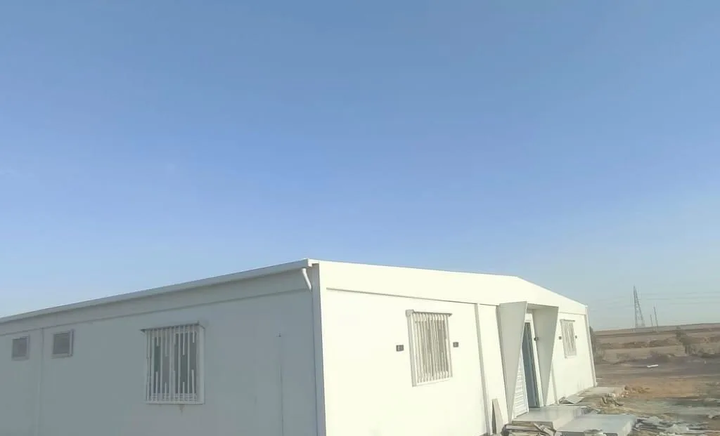 مجمع كرفانات ساندوتش بانل أبيض طويل بنوافذ بحماية حديد مركّب في موقع عمل صحراوي