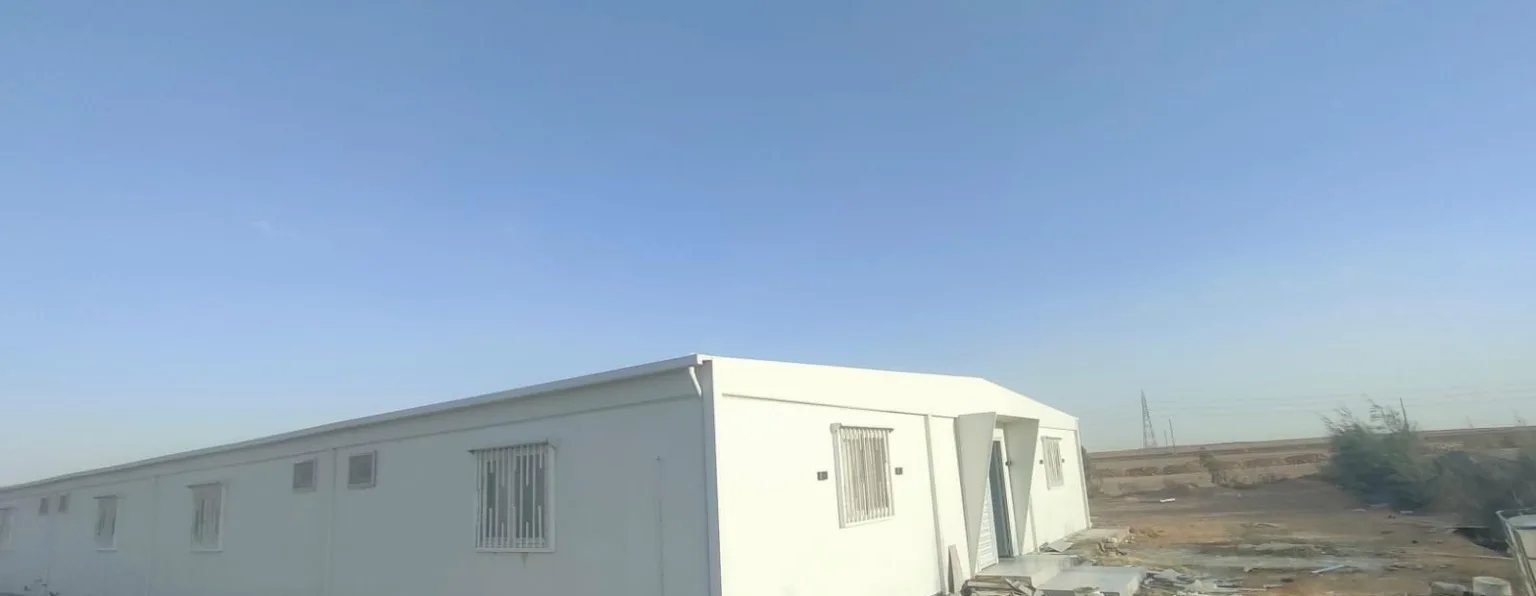 مجمع كرفانات ساندوتش بانل أبيض طويل بنوافذ بحماية حديد مركّب في موقع عمل صحراوي