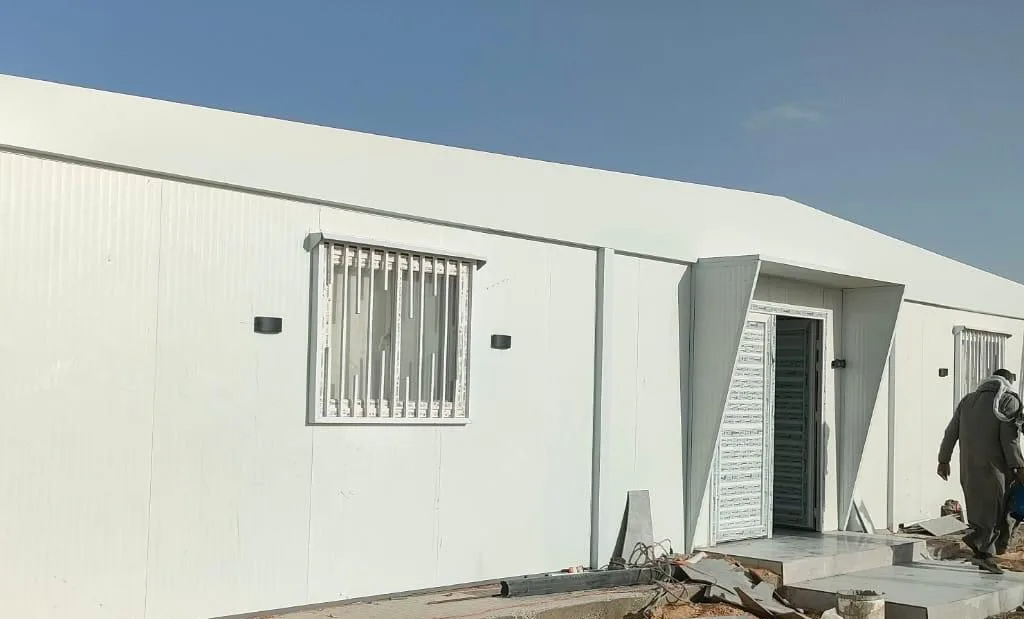 مدخل مجمع كرفانات أبيض بدرجات وعمال ينهون التشطيب الخارجي بعد التركيب