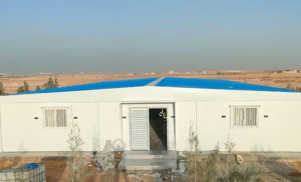 واجهة مجمع كرفانات أبيض بمدخل رئيسي ونوافذ جانبية في موقع مشروع صحراوي