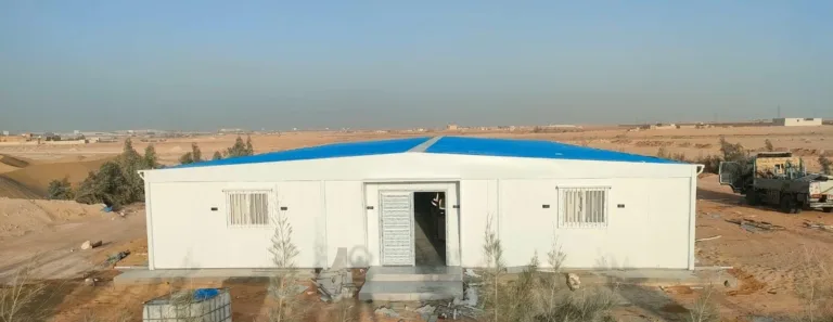 واجهة مجمع كرفانات أبيض بمدخل رئيسي ونوافذ جانبية في موقع مشروع صحراوي