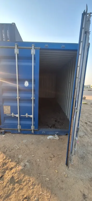 حاوية شحن 20 قدم زرقاء بباب مفتوح يظهر منه الداخل في ساحة رملية