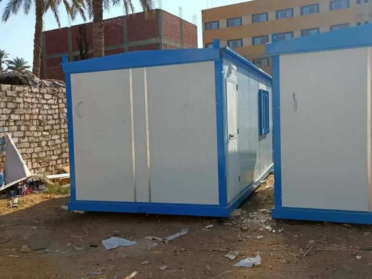 كرفان ساندوتش بانل أبيض بإطار أزرق وباب مزدوج بجوار كرفان آخر في ساحة ترابية