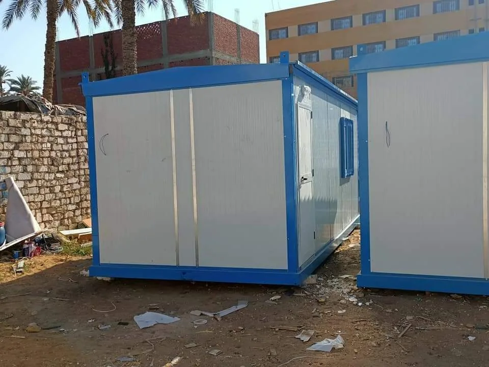 كرفان ساندوتش بانل بإطار أزرق وباب مزدوج على أرض رملية بجوار كرفان آخر