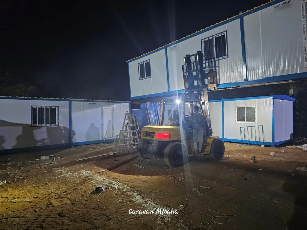 موقع تركيب ليلي: كرفان دورين ساندوتش بانل بإطار أزرق، ورافعة شوكية، وكرفان صغير بجواره